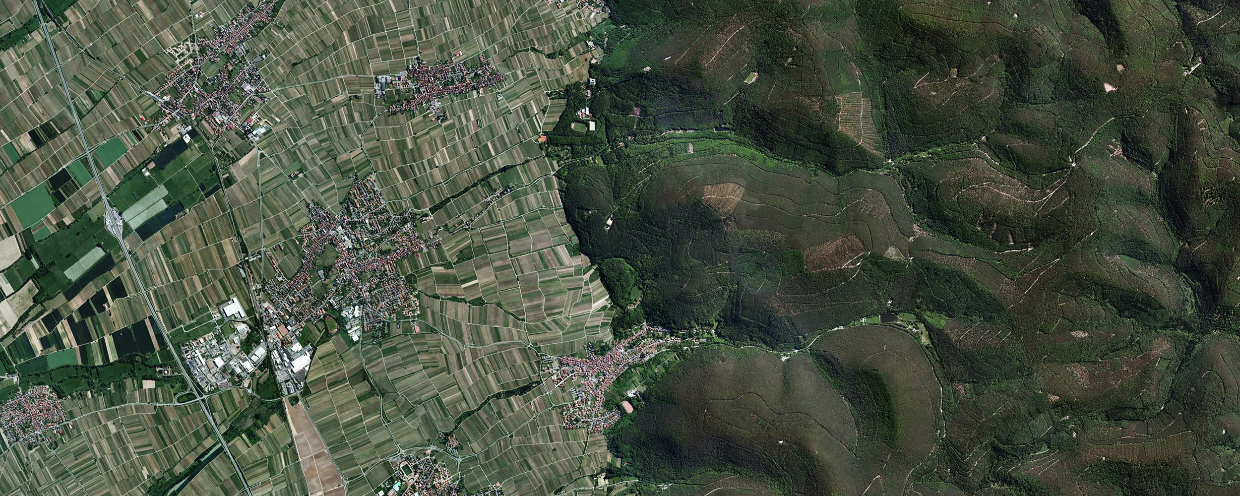 Satellite view of agricultural land and villages meeting forested hills