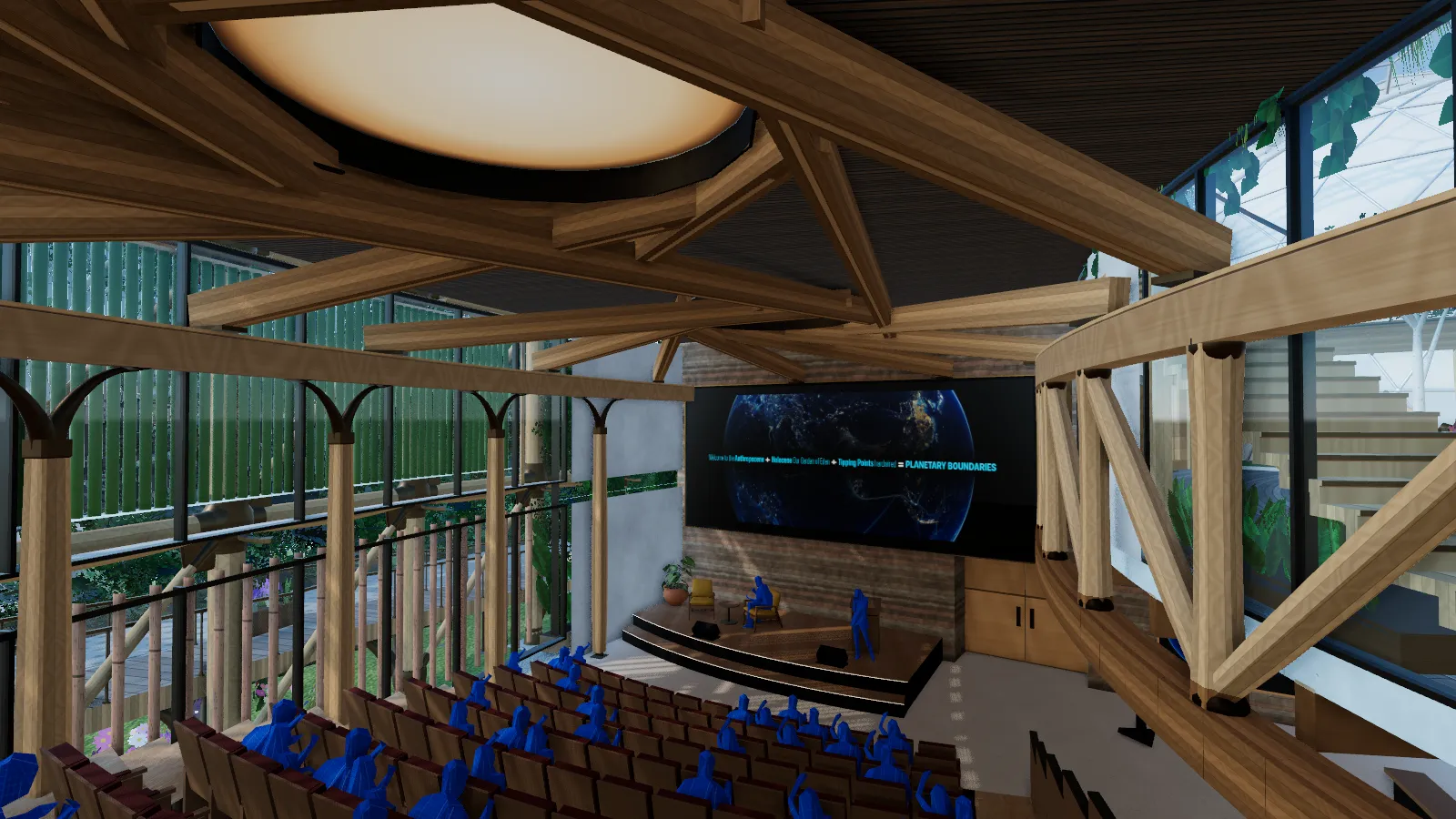 From the top row of a full raked hall, a stage and a wide screen under a woven timber roof.
